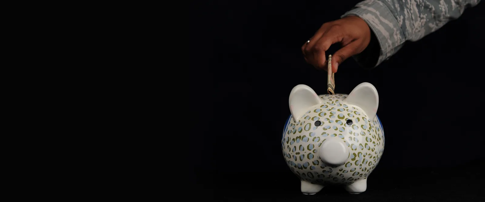 Airman dropping a folded bill into a piggy bank